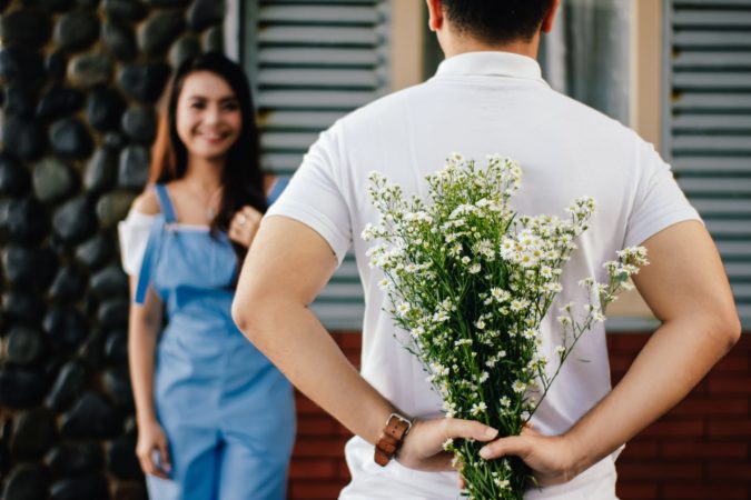 Un homme tenant des fleurs derrière son dos tandis qu'une dame le salue.