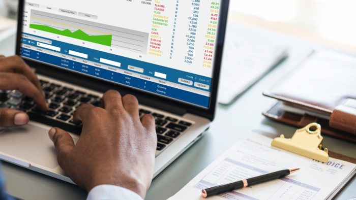 Un hombre introduciendo números en un informe financiero en un portátil.