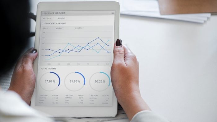 Una mujer sosteniendo una tableta con un informe financiero en la pantalla.