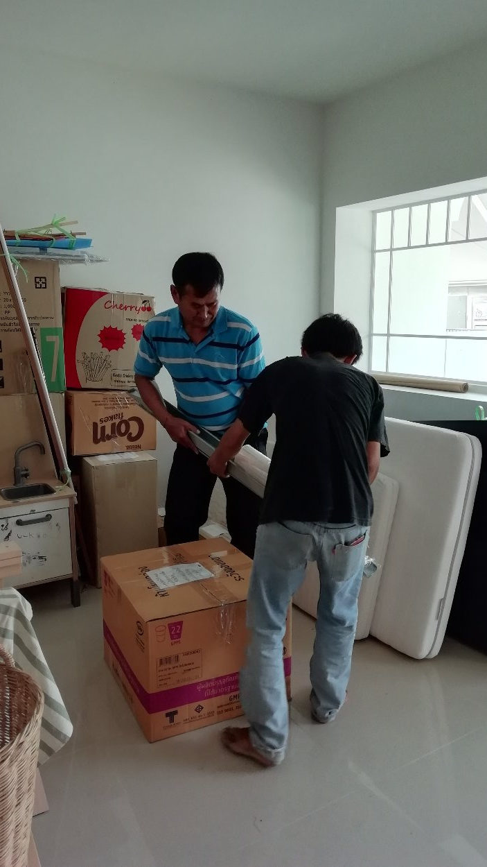 Movers wrapping a box with plastic in a living room.
