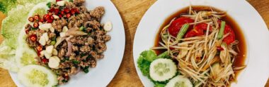 A plate of som tam (green papaya salad) and a plate of larb on a wooden table