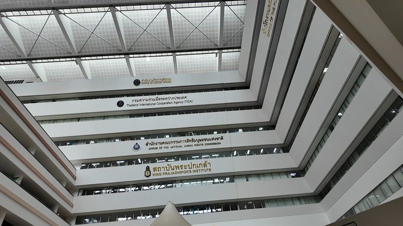 Atrium of a Thai government complex with agency name signs on each floor