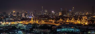 The Grand Palace lit up at night with the Bangkok skyline behind it