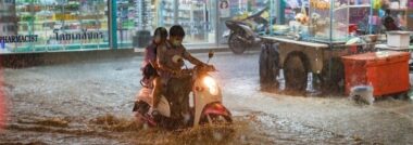 Motorcycle riders crossing a flooded Bangkok street at night
