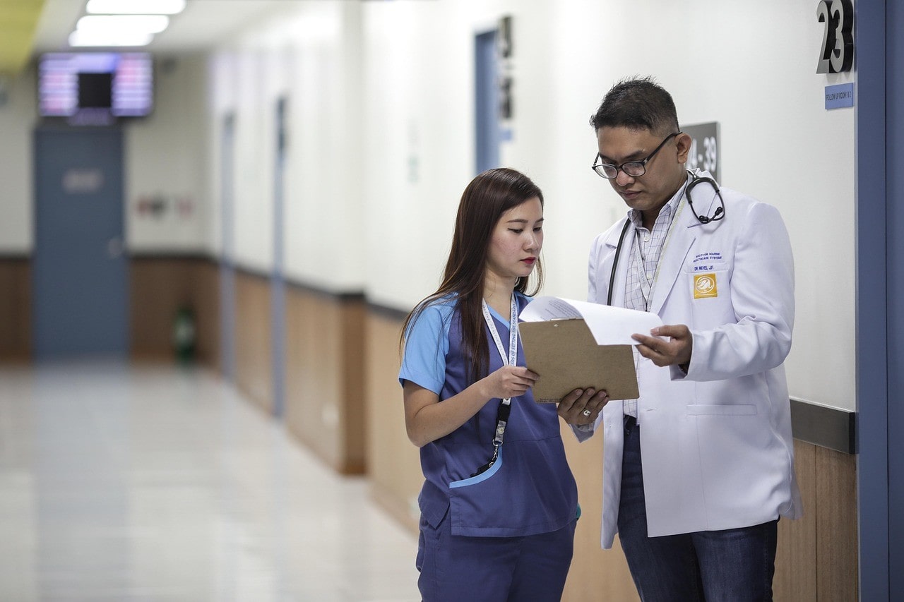 A doctor and nurse reviewing a patient's clipboard together in a hospital corridor