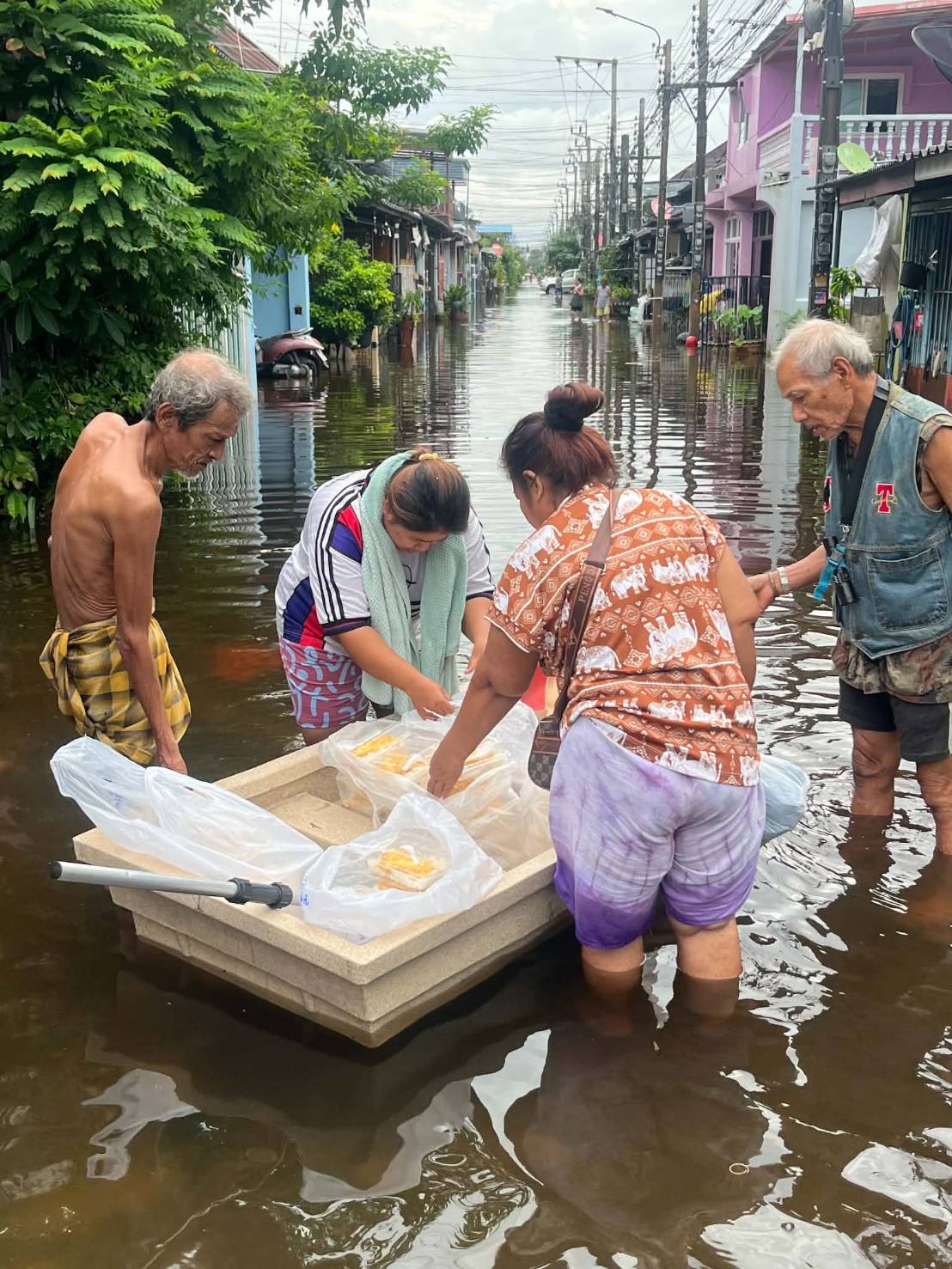 Elderly residents and neighbors wading through floodwater to deliver food aid in Bangkok