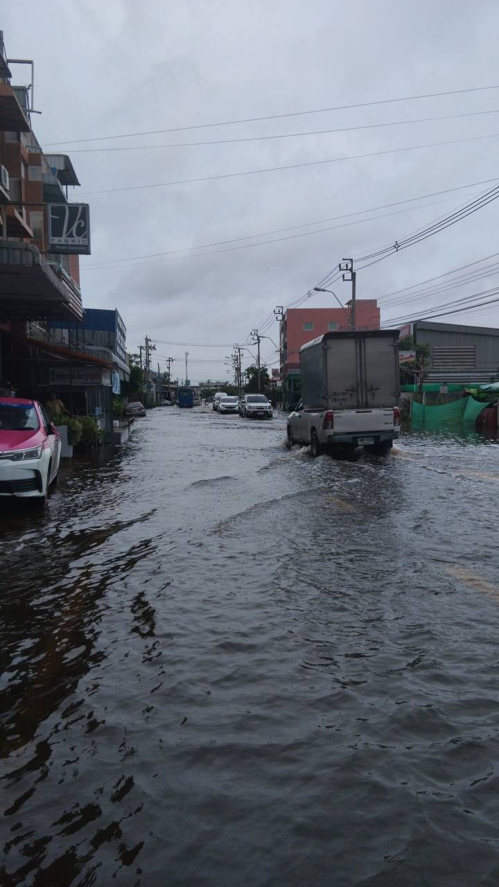Flooded Bangkok street with cars and a pickup truck driving through standing water