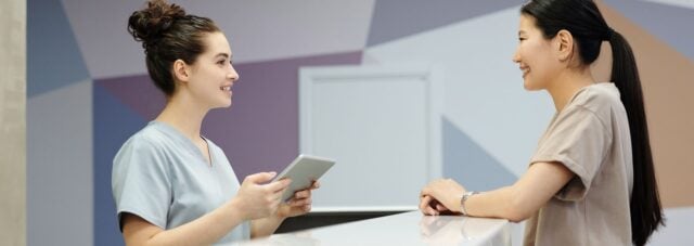 Clinic reception staff reviewing details with a patient at the counter