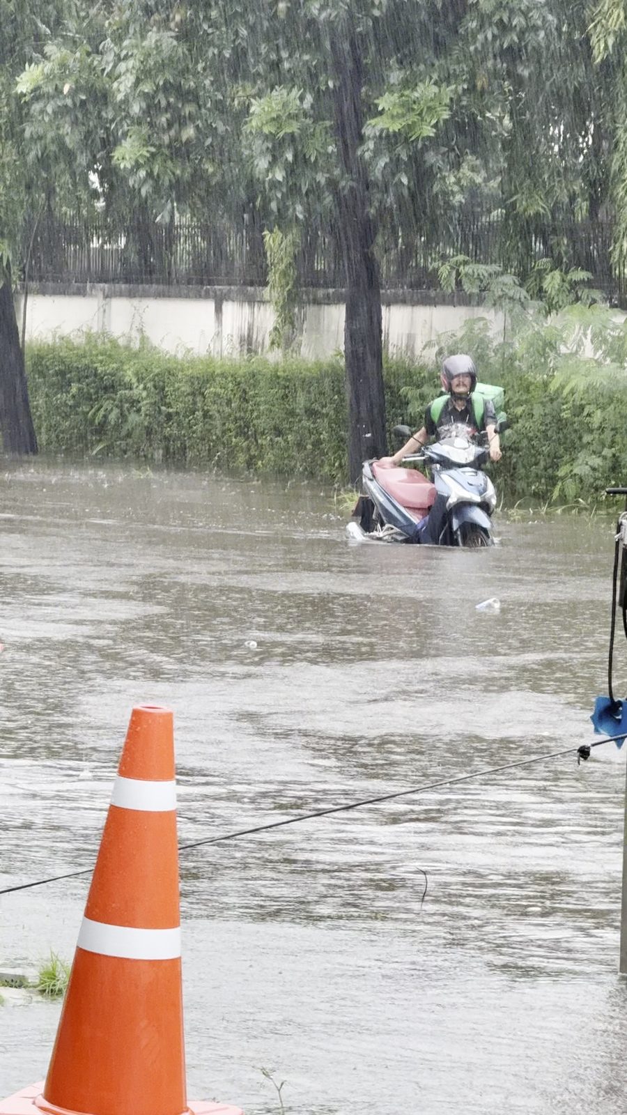 Motorcycle rider wading through a flooded road in heavy rain