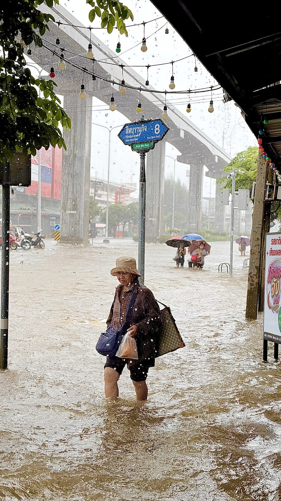 Woman wading through deep floodwater in the rain in Min Buri, Bangkok
