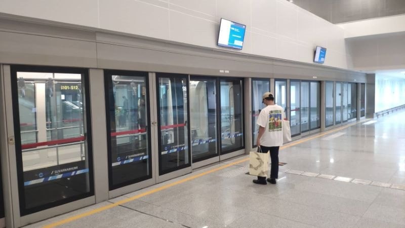 Passenger with shopping bags waiting at the glass screen doors of an Airport Rail Link City Line platform in Bangkok
