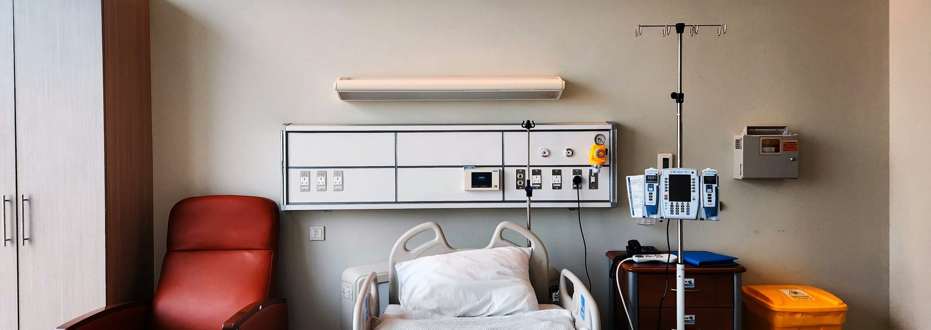 Private hospital room with bed, armchair and IV stand