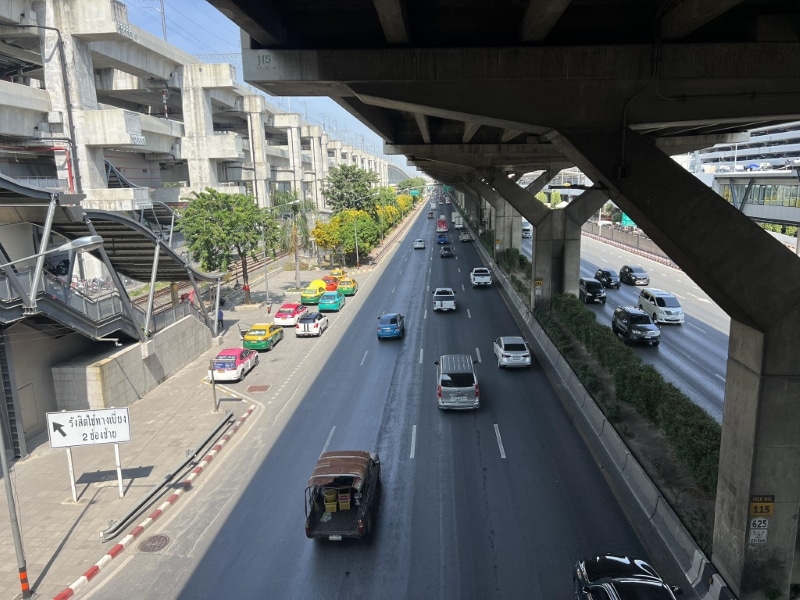 Taxis waiting at the curb on the road outside Don Mueang Airport, under the elevated expressway