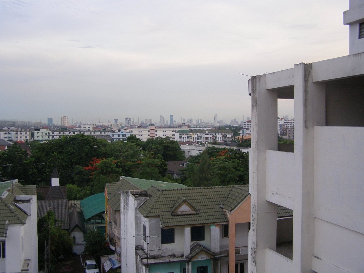 Townhouses below an older apartment block in low-rise Bangkok, city towers on the horizon