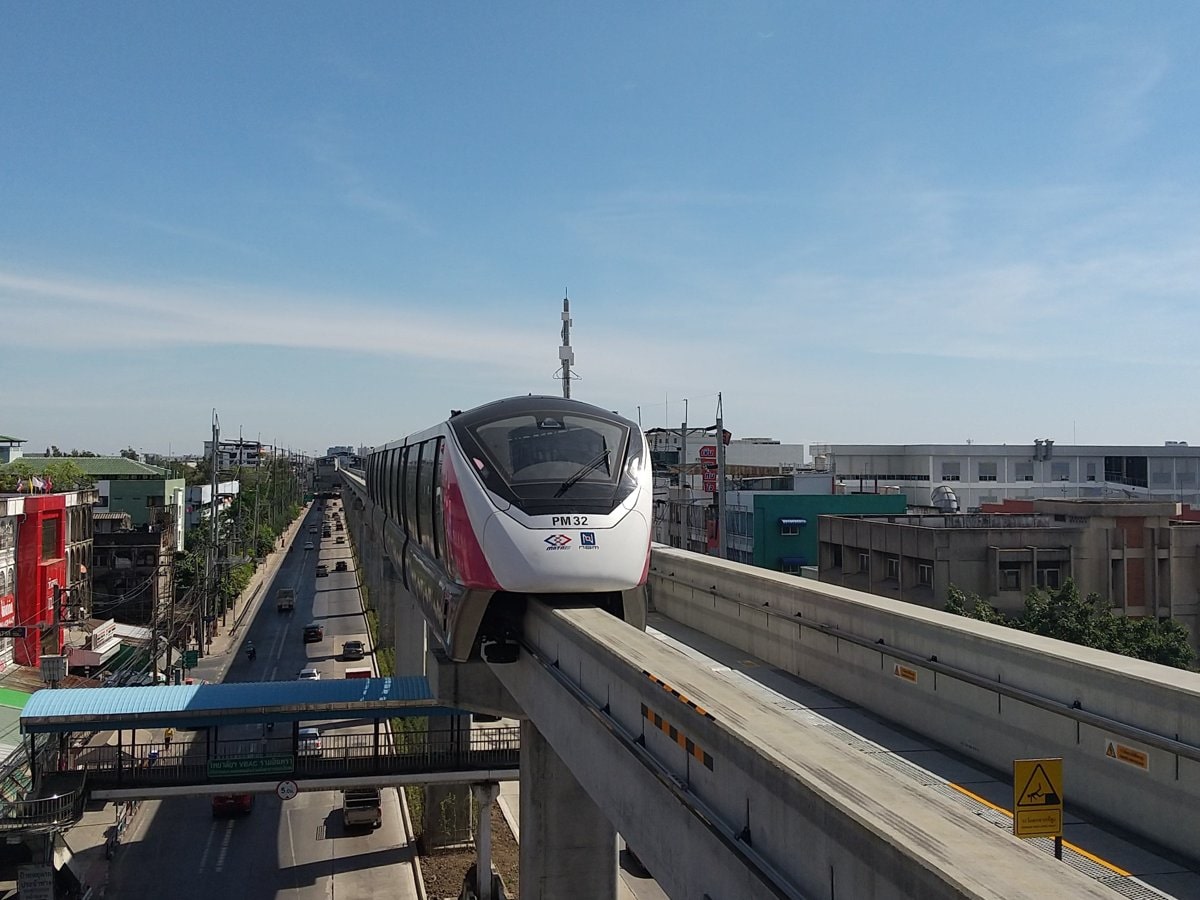 An MRT Pink Line train arriving at Ram Inthra Kor Mor 4 station above Ram Inthra Road, with a footbridge and traffic below