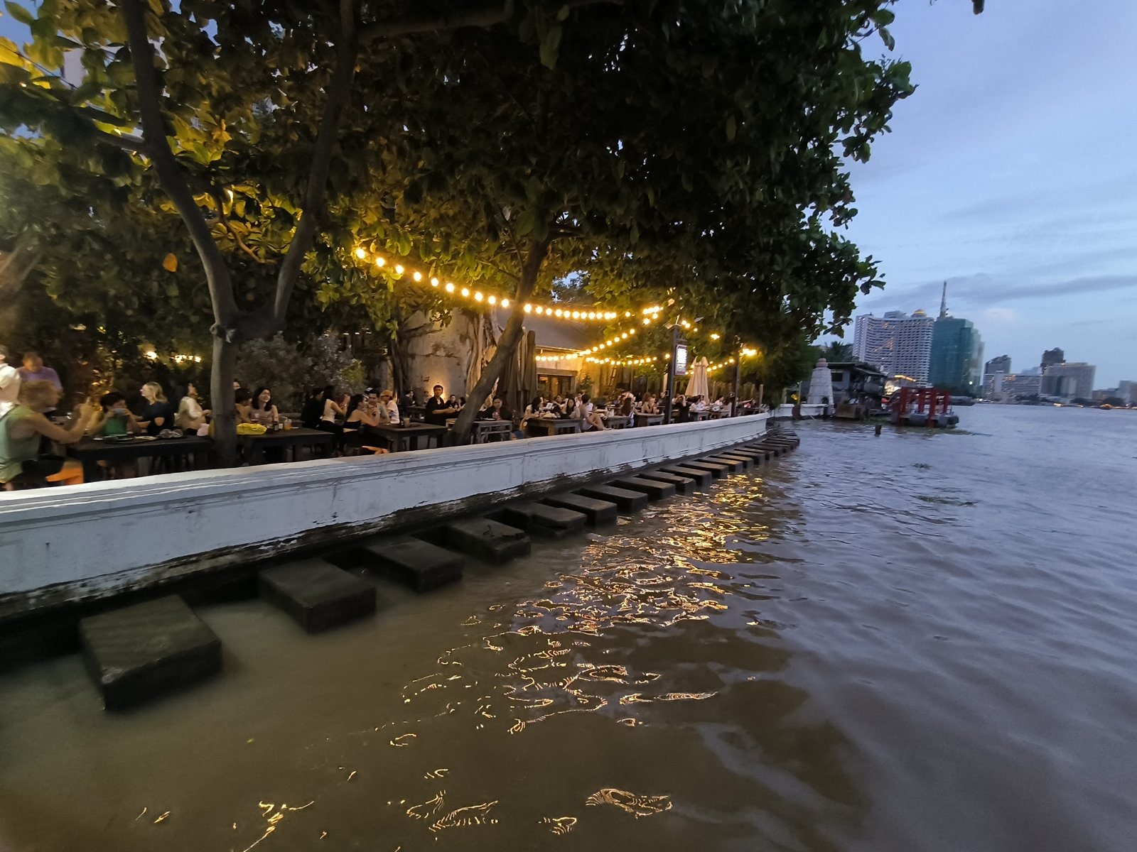 Riverside cafe tables under string lights on the Chao Phraya in Talad Noi, Bangkok
