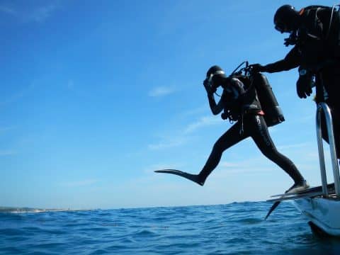 A person wearing scuba diving equipment stepping off a boat and into the water.